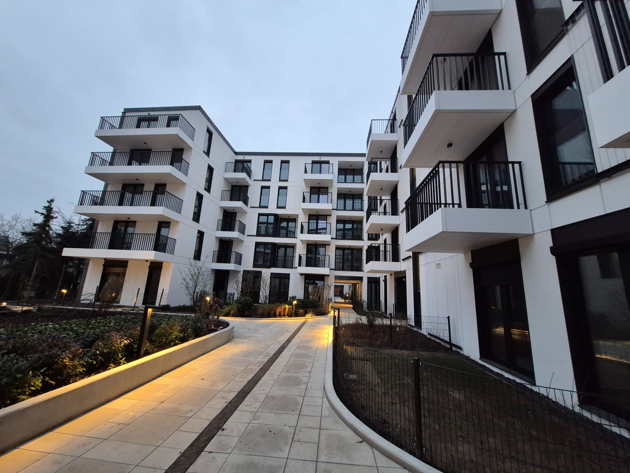 Nowoczesny budynek wielorodzinny z balkonami, oświetlony ścieżkami, widziany z perspektywy niskiego kąta, podkreślającego jego architekturę i oświetlenie.