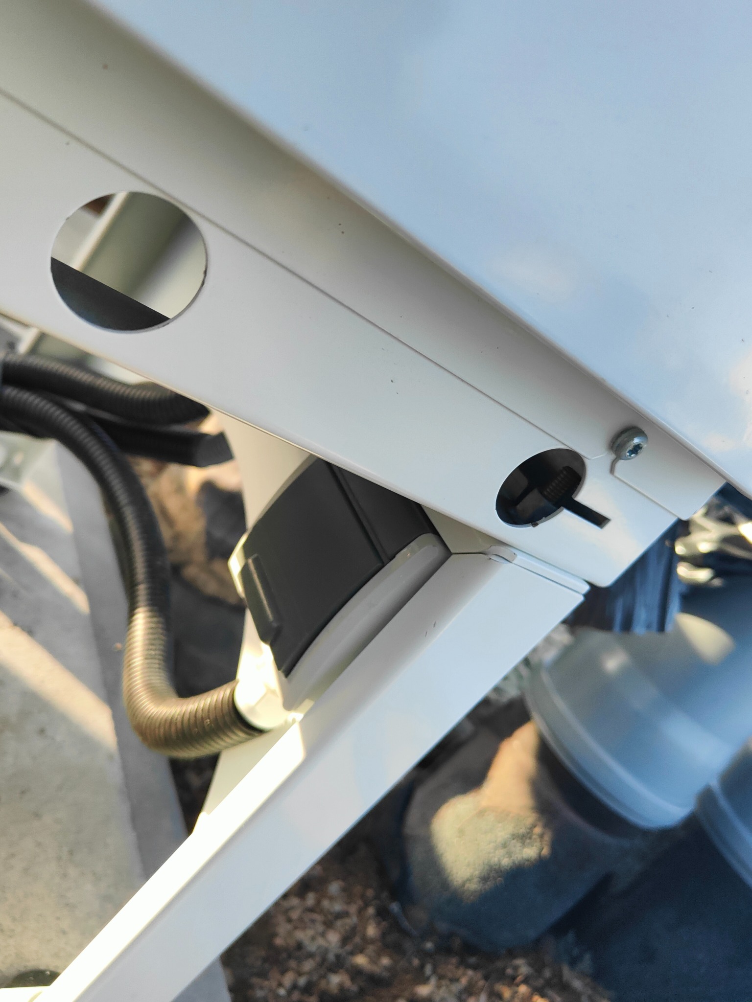 Biała konstrukcja z widoczną czarną rurą karbowaną i otworem z przewodem, potencjalnie element instalacji elektrycznej lub domofonu.