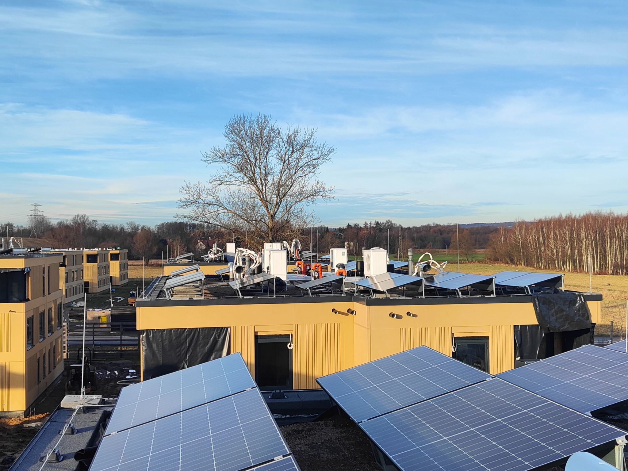 Instalacja paneli słonecznych na dachach budynków w słoneczny dzień. Widoczny krajobraz z drzewami w tle.  Energia odnawialna w zabudowie modułowej.