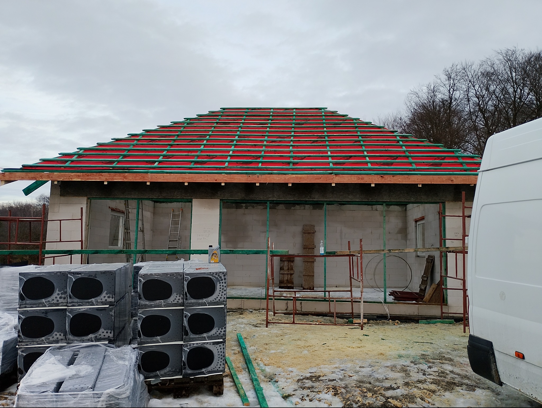 Budowa domu jednorodzinnego: ściany z betonu komórkowego, czerwona membrana dachowa i zielone łaty. Na pierwszym planie bloczki styropianowe.