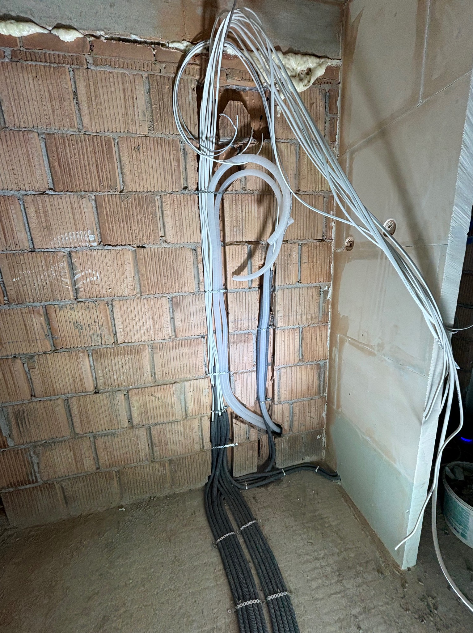 Wewnętrzna instalacja elektryczna w trakcie montażu: kable w peszlach prowadzone wzdłuż ceglanej ściany i podłoża, widoczne puszki instalacyjne w ścianie. Etap prac wykończeniowych.