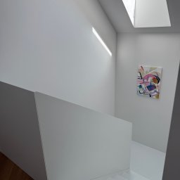 PRACOWNIA PROJEKTOWA KAMIL BUBEL - Minimalistyczne wnętrze: białe schody z drewnianym akcentem, abstrakcyjny obraz na ścianie, doświetlone oknem dachowym. Nowoczesny design.