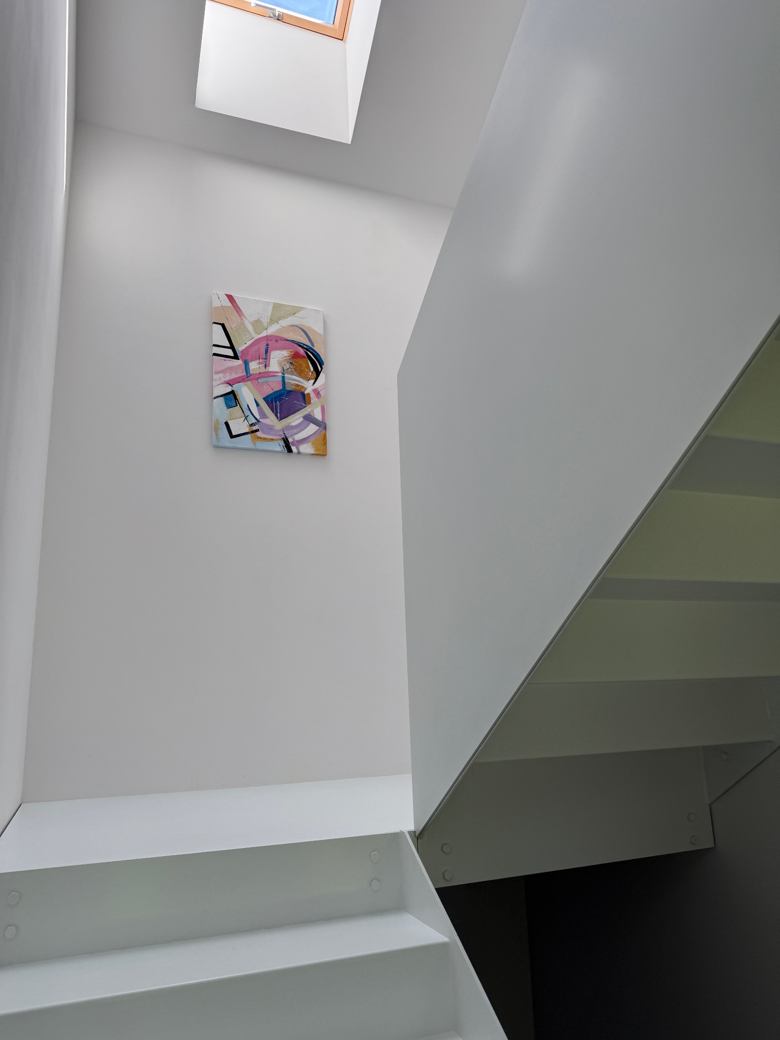 Minimalistyczne wnętrze: białe schody z przeszkloną barierką, abstrakcyjny obraz na ścianie i okno dachowe wpadające w kadr. Nowoczesny design.