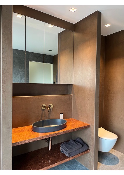 Nowoczesna łazienka z umywalką nablatową w kształcie elipsy, brązowymi płytkami i lustrem wbudowanym w szafkę. Uwagę przykuwa unikalny blat z widocznym usłojeniem.