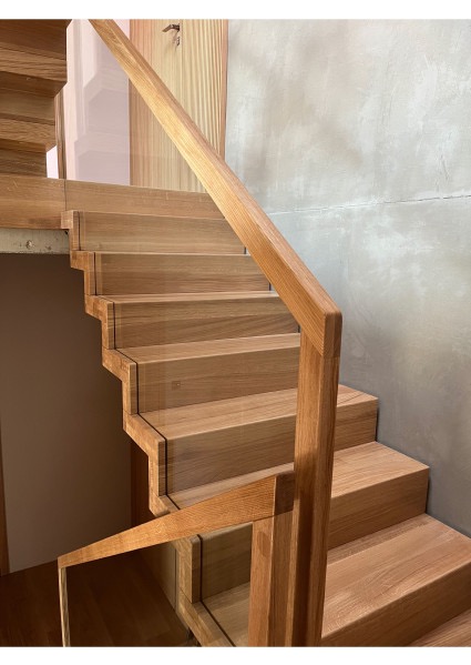 Drewniane schody z balustradą na betonowej ścianie. Stopnie schodów z wyraźnymi krawędziami. Dolne stopnie z ukrytymi schowkami. Minimalistyczny design.