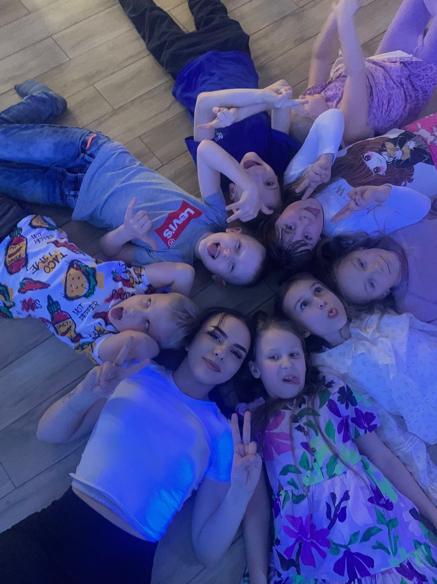 Animator z grupą dzieci leżących w kole na podłodze w Nowogardzie. Dzieci ubrane w kolorowe ubrania, robią śmieszne miny i pokazują znaki palcami.