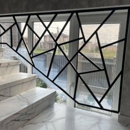 Integralstal Serhii Bondarenko - Nowoczesna, czarna balustrada schodowa z geometrycznym wzorem trójkątów, zamontowana przy marmurowych schodach z widokiem na okno i zewnętrzny krajobraz.