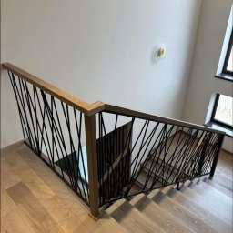 Integralstal Serhii Bondarenko - Nowoczesne schody z poręczą o geometrycznym wzorze, drewniane stopnie i podłoga, widok z góry. Metalowe pręty tworzą unikalny design.