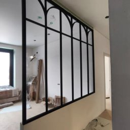 Integralstal Serhii Bondarenko - Nowoczesna zabudowa ścianki działowej z czarną metalową ramą i szklanymi panelami w stylu loftowym, widoczna w jasnym wnętrzu w trakcie wykańczania.