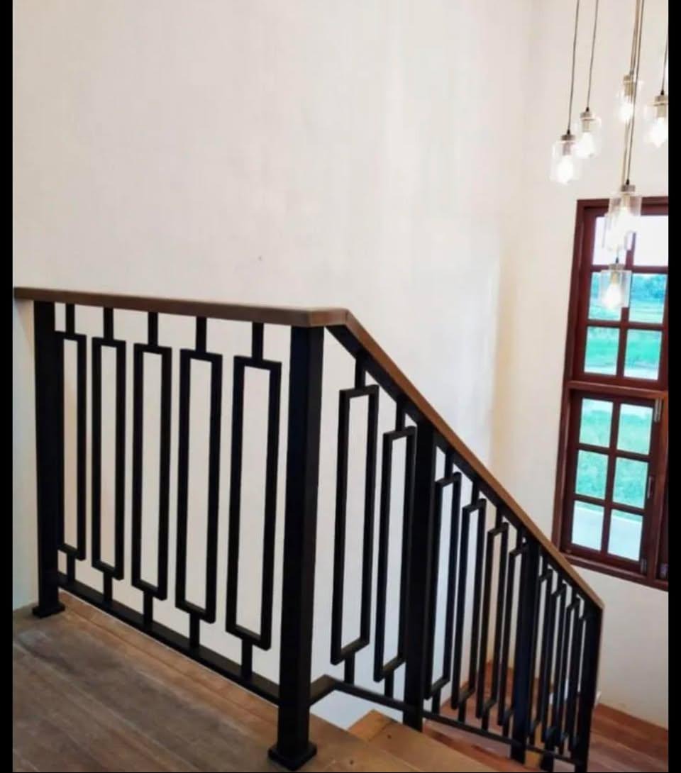 Nowoczesna poręcz schodowa z czarnymi, geometrycznymi elementami i drewnianym wykończeniem, oświetlona przez wiszące lampy. Widok z dołu schodów.