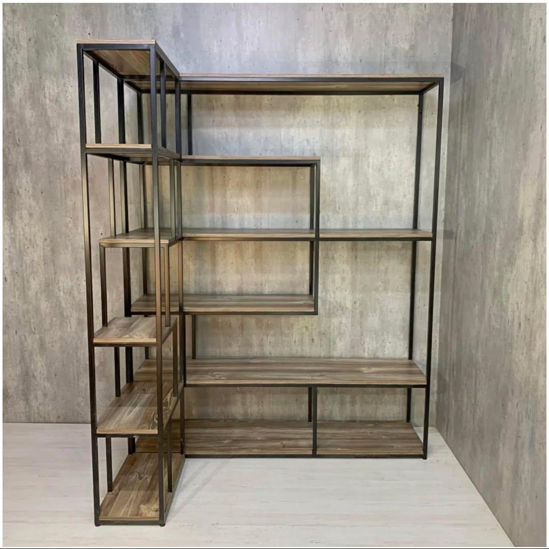 Loftowy regał z metalowym stelażem i drewnianymi półkami na tle betonowej ściany. Asymetryczna konstrukcja, minimalistyczny design, industrialny styl.