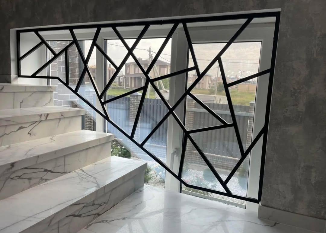 Nowoczesna, czarna balustrada schodowa z geometrycznym wzorem trójkątów, zamontowana przy marmurowych schodach z widokiem na okno i zewnętrzny krajobraz.