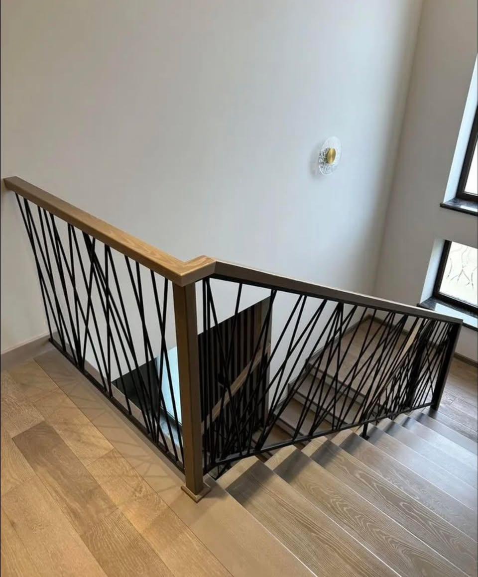 Nowoczesne schody z poręczą o geometrycznym wzorze, drewniane stopnie i podłoga, widok z góry. Metalowe pręty tworzą unikalny design.