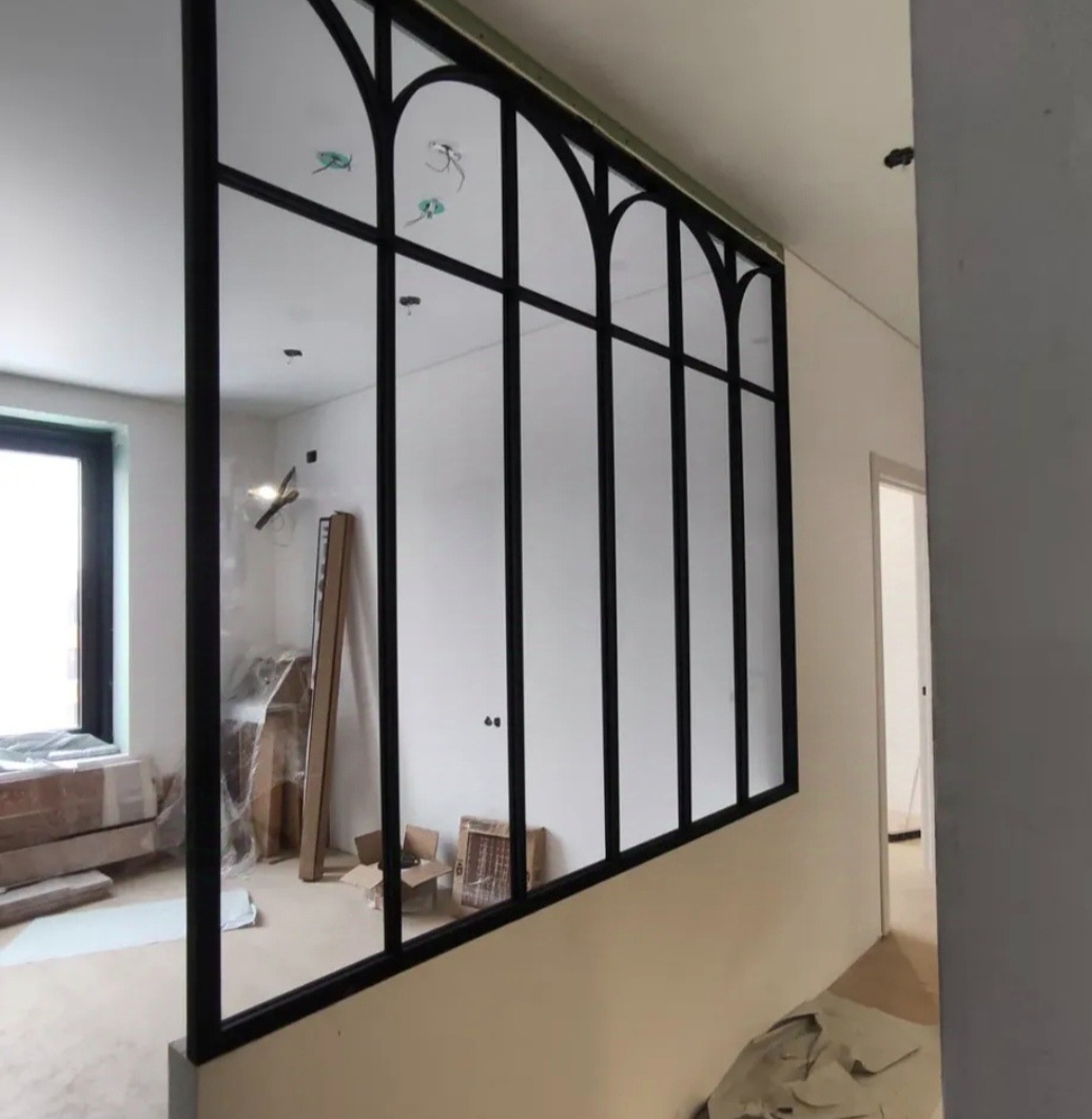 Nowoczesna zabudowa ścianki działowej z czarną metalową ramą i szklanymi panelami w stylu loftowym, widoczna w jasnym wnętrzu w trakcie wykańczania.