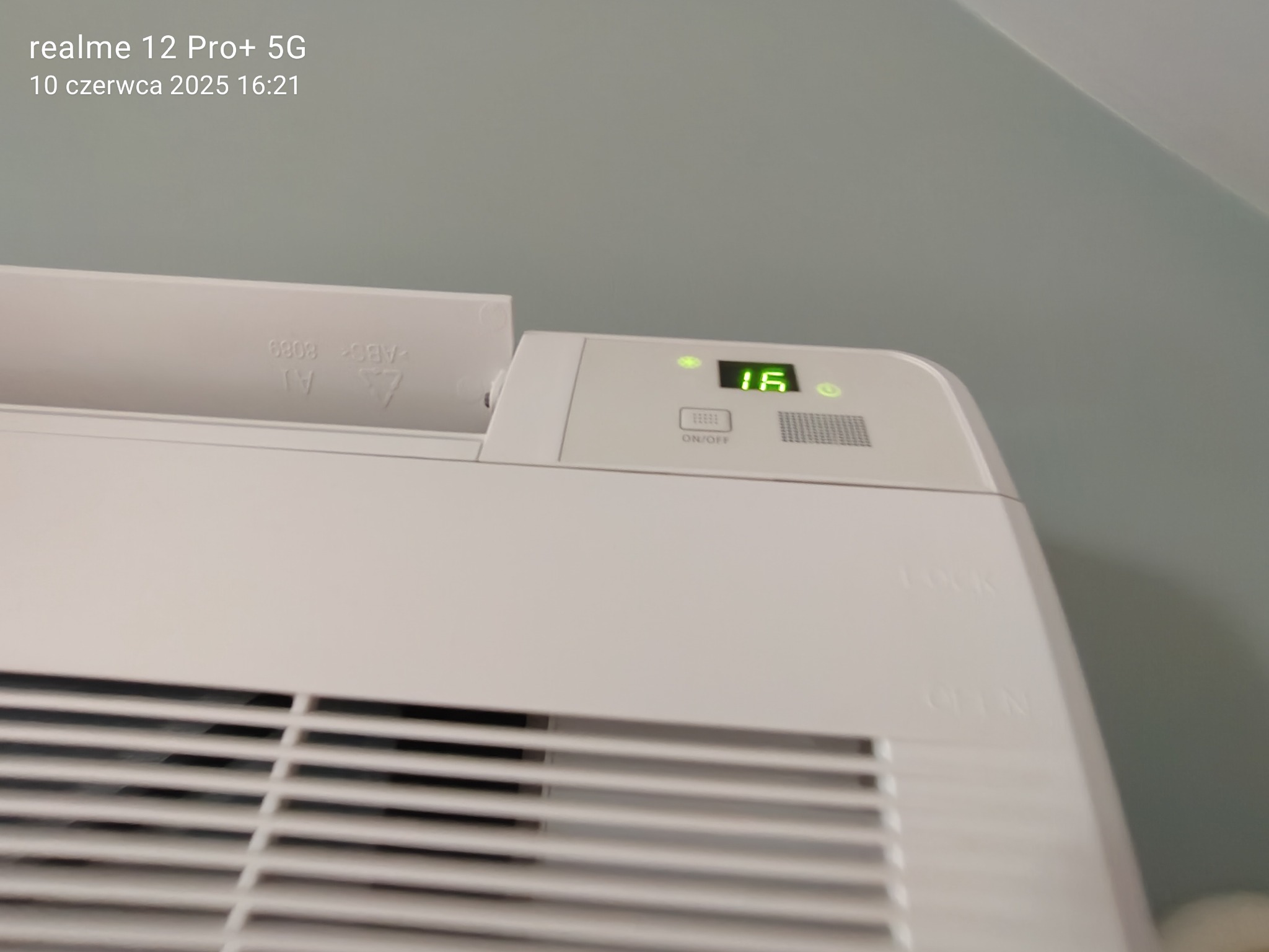 Biały klimatyzator ścienny z wyświetlaczem LED wskazującym temperaturę 16 stopni Celsjusza, widoczne kratki wentylacyjne i przyciski sterujące.
