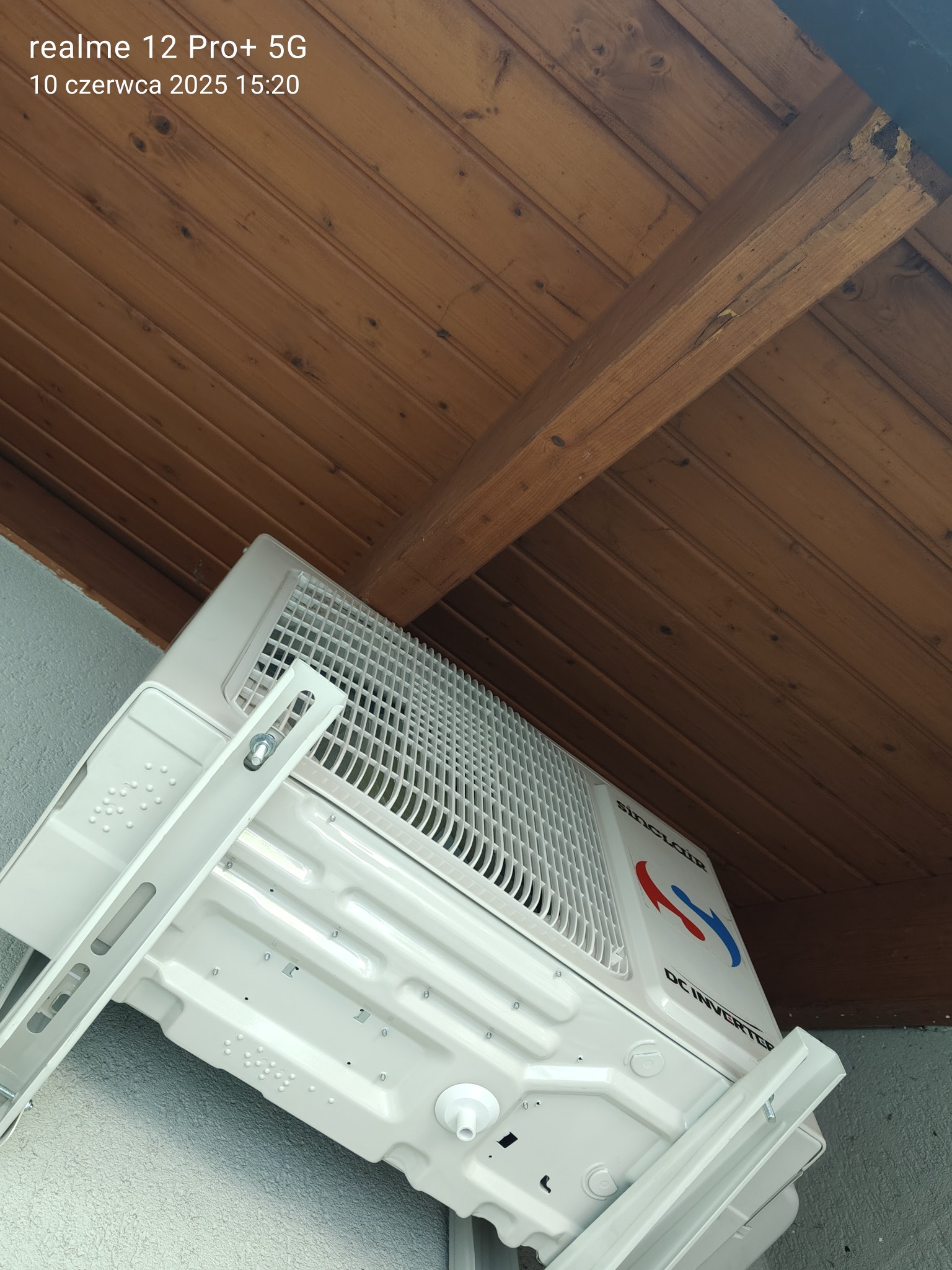 Biała klimatyzacja Sinclair DC Inverter zamontowana pod drewnianym sufitem, widoczna z dołu pod kątem. Widoczne mocowania i logo producenta.