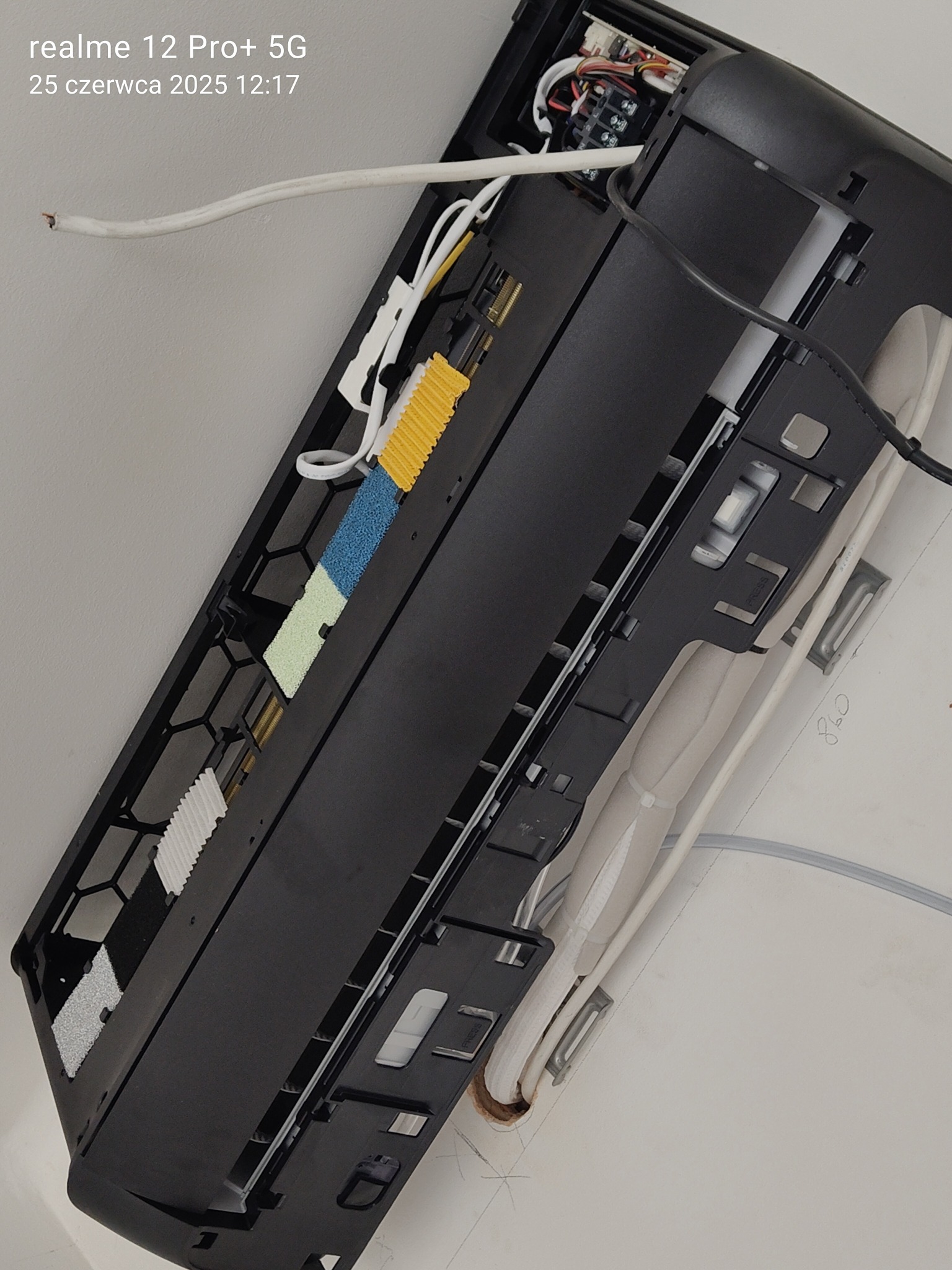 Czarny klimatyzator ścienny w trakcie serwisu, widoczne filtry i okablowanie. Zdjęcie z bliska, ukazujące szczegóły konstrukcji i podłączenia.