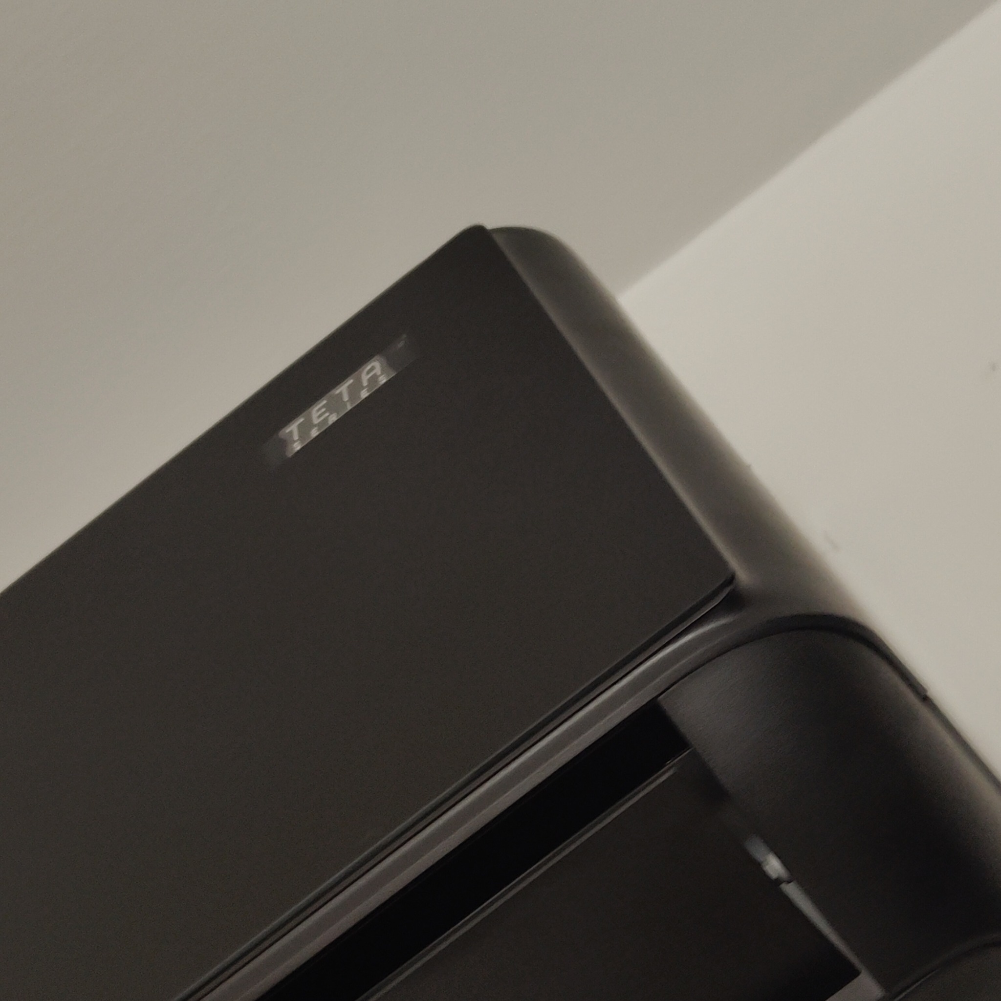 Czarny klimatyzator z widocznym napisem 'TETA' na obudowie, zamontowany przy białym suficie, sfotografowany pod kątem.
