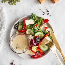 Perfect Chef Catering Dietetyczny Warszawa Dieta Pudełkowa - Świeża sałatka z serem camembert, czerwoną papryką i ogórkiem, z sosem w szklanej miseczce na marmurowym tle, z dodatkiem złotych sztućców i przypraw.