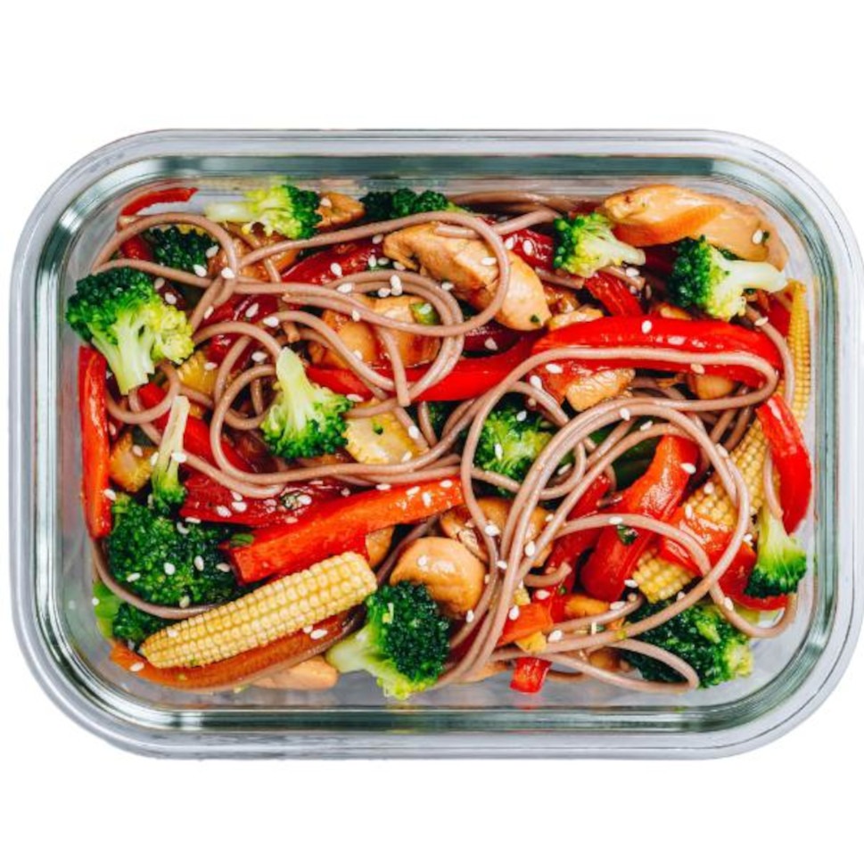 Lunchbox z brązowym makaronem, brokułami, papryką i kukurydzą, posypany sezamem, w szklanym pojemniku. Zdrowy posiłek gotowy do spożycia.