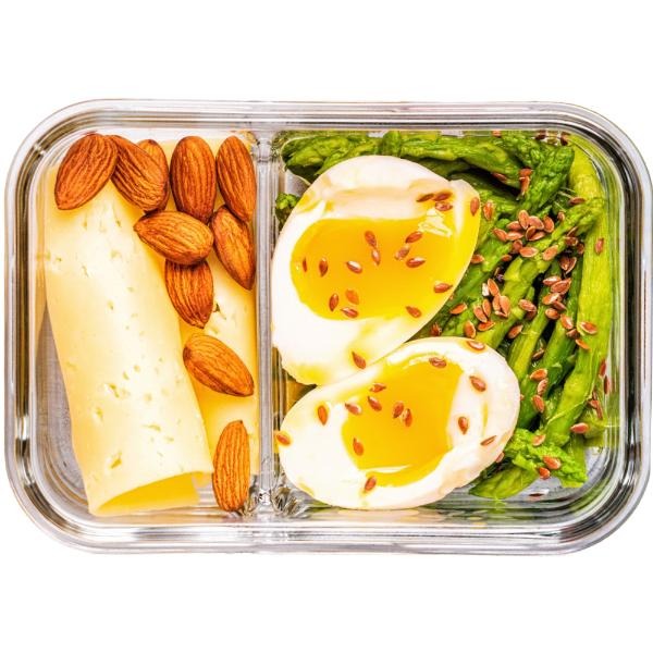Lunchbox z dietetycznym posiłkiem: ser, migdały, szparagi i jajka na miękko posypane siemieniem lnianym. Zdrowy catering w szklanym pojemniku.
