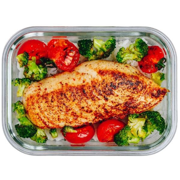 Pudełko z cateringiem dietetycznym: kurczak z przyprawami, ryżem, brokułami i pieczonymi pomidorami. Całość w szklanym pojemniku.