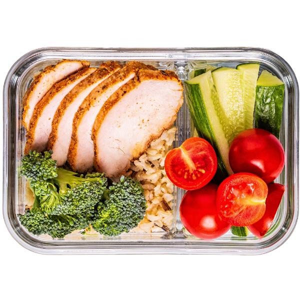 Dietetyczny posiłek w szklanym pojemniku: grillowany kurczak, ryż, brokuły, ogórek i pomidory. Zdrowy lunchbox z podziałem na sekcje.