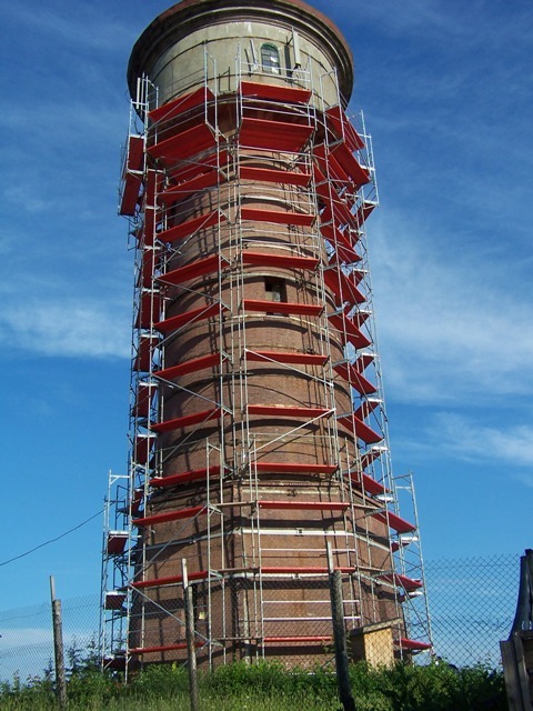 Wieża ciśnień w rusztowaniach DELTA z czerwonymi podestami, widok z dołu na błękitne niebo. Rusztowania budowlane z Olecka.