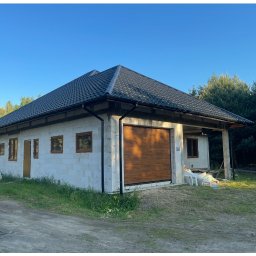 Tomasz Gałus - Niedokończony budynek z dachem z blachy na tle zieleni, widoczne okna i brama garażowa. Budynek w stanie surowym, ściany z bloczków.