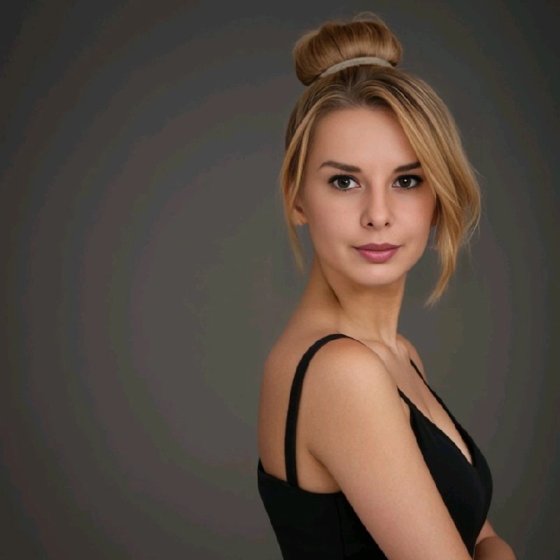 Portret młodej kobiety z blond włosami upiętymi w kok, ubrana w czarny top na tle szarego studia. Delikatny makijaż, spojrzenie w bok.