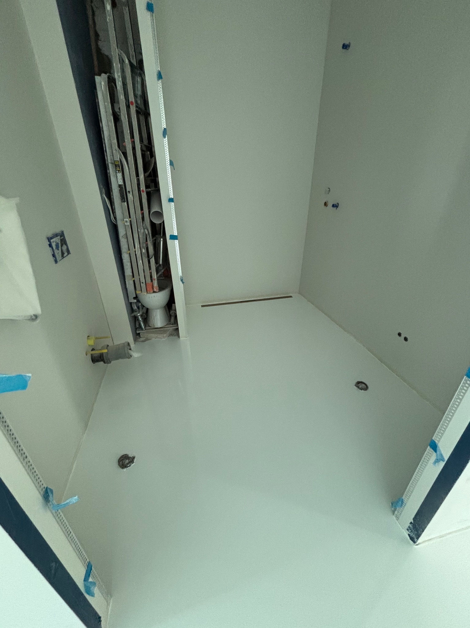 Jasna, gładka posadzka w łazience w trakcie remontu, widoczne instalacje i drabina oparta o ścianę. Minimalistyczny design i świeżo położona powierzchnia.