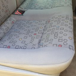 Flame Mariusz Wnuk - Wnętrze pojazdu: wyprana tapicerka tylnej kanapy z wzorem w geometryczne kształty i symbole, widoczny pas bezpieczeństwa i fragment podłogi.