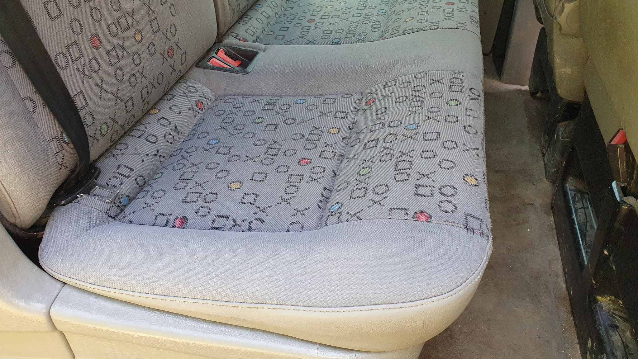 Wnętrze pojazdu: wyprana tapicerka tylnej kanapy z wzorem w geometryczne kształty i symbole, widoczny pas bezpieczeństwa i fragment podłogi.