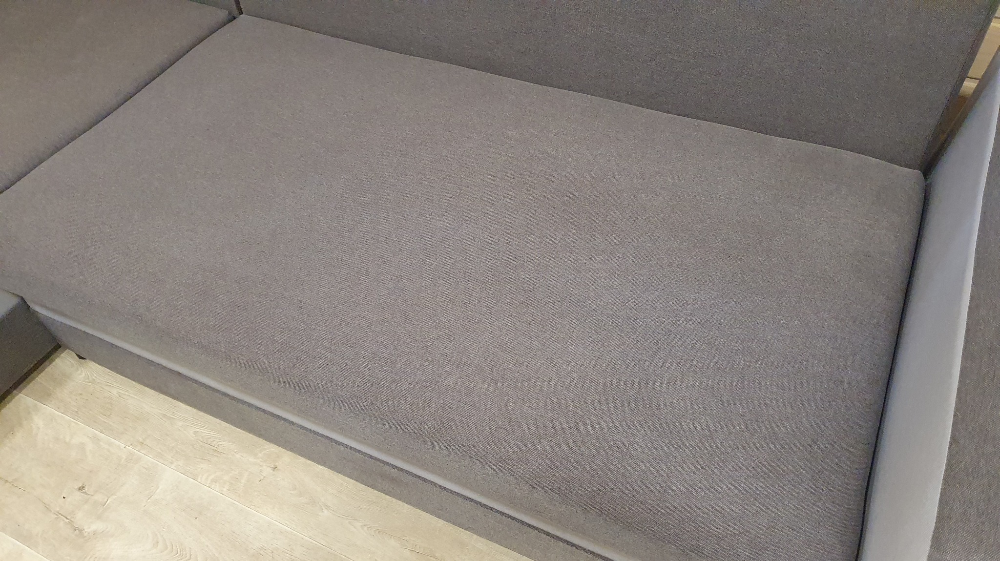 Szary narożnik po czyszczeniu, widoczna faktura materiału i jasna podłoga. Czysta tapicerka, brak plam. Ujęcie z góry, wypełniające kadr.