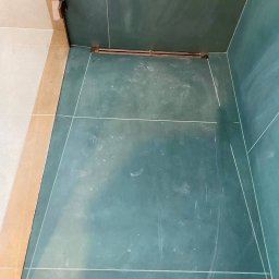 Pomalowany Wrocław - Wykończona wnęka prysznicowa z zielonymi płytkami, widoczne fugi i odpływ liniowy. Górny kadr.