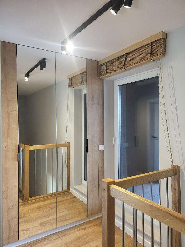 Nowoczesne wykończenie korytarza z lustrami, drewnianą balustradą i oknami z bambusowymi roletami. Oświetlenie punktowe podkreśla detale.