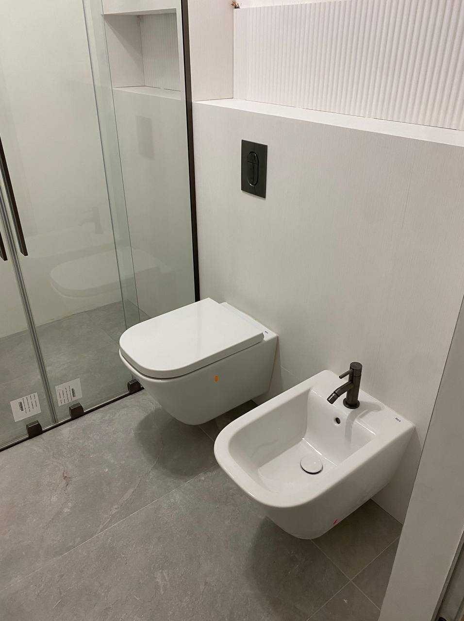 Nowoczesna łazienka z podwieszaną miską WC i bidetem na szarych płytkach, minimalistyczny design, czarne detale, szklana kabina prysznicowa.