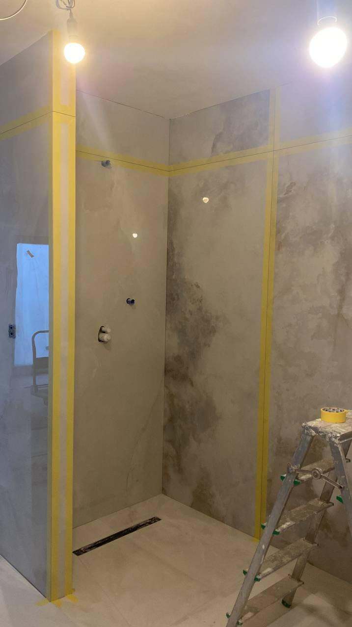 Wykończona kabina prysznicowa z efektem dekoracyjnym na ścianach, zabezpieczona taśmą malarską, z widoczną drabinką i odpływem liniowym w podłodze.