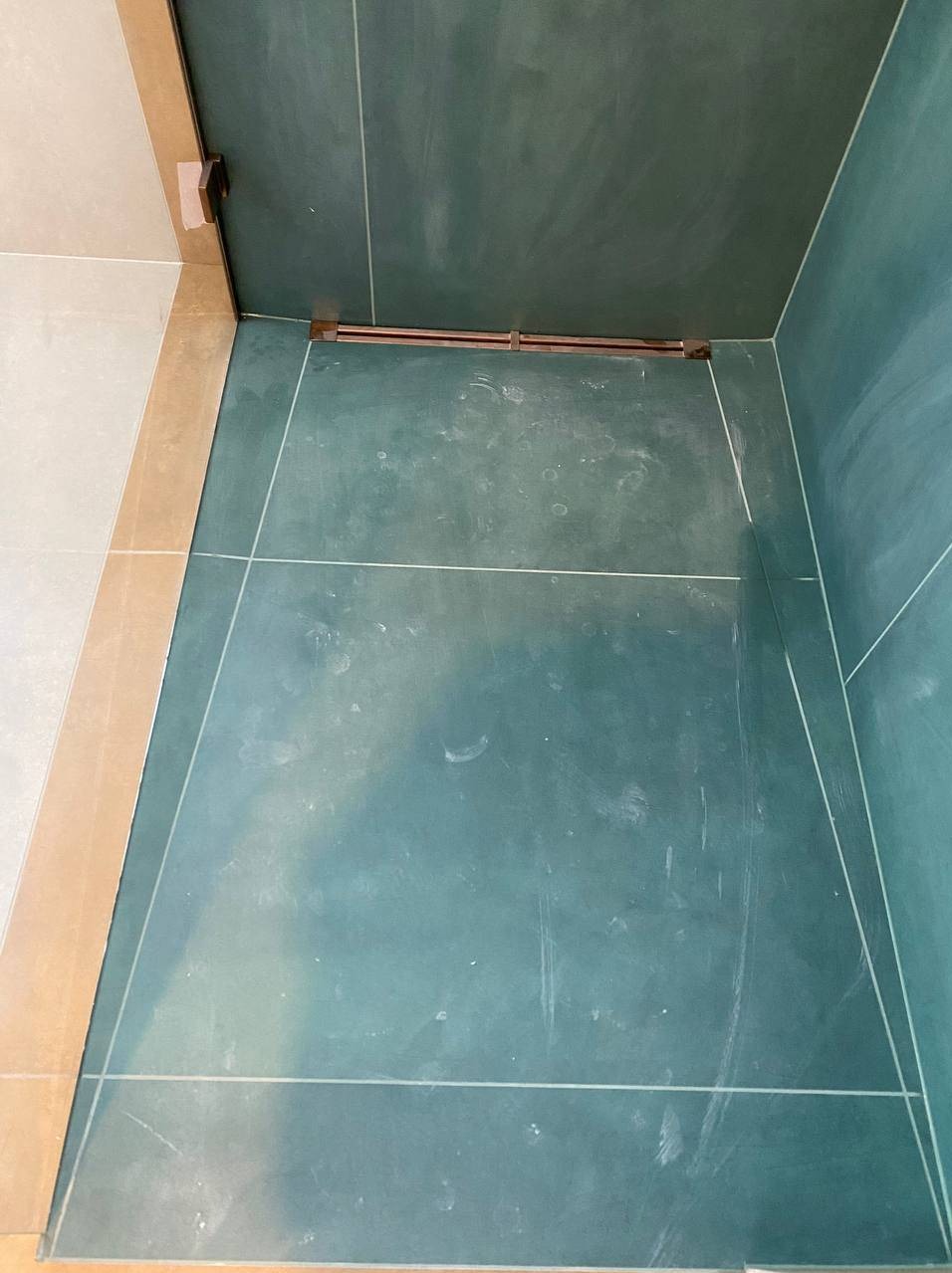 Wykończona wnęka prysznicowa z zielonymi płytkami, widoczne fugi i odpływ liniowy. Górny kadr.