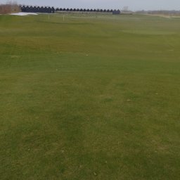 Marek Kolański Ogrody - Rozległy trawnik golfowy z rzędem charakterystycznych, ciemnych budek na horyzoncie. Częściowo pokryty śniegiem, pochmurne niebo.