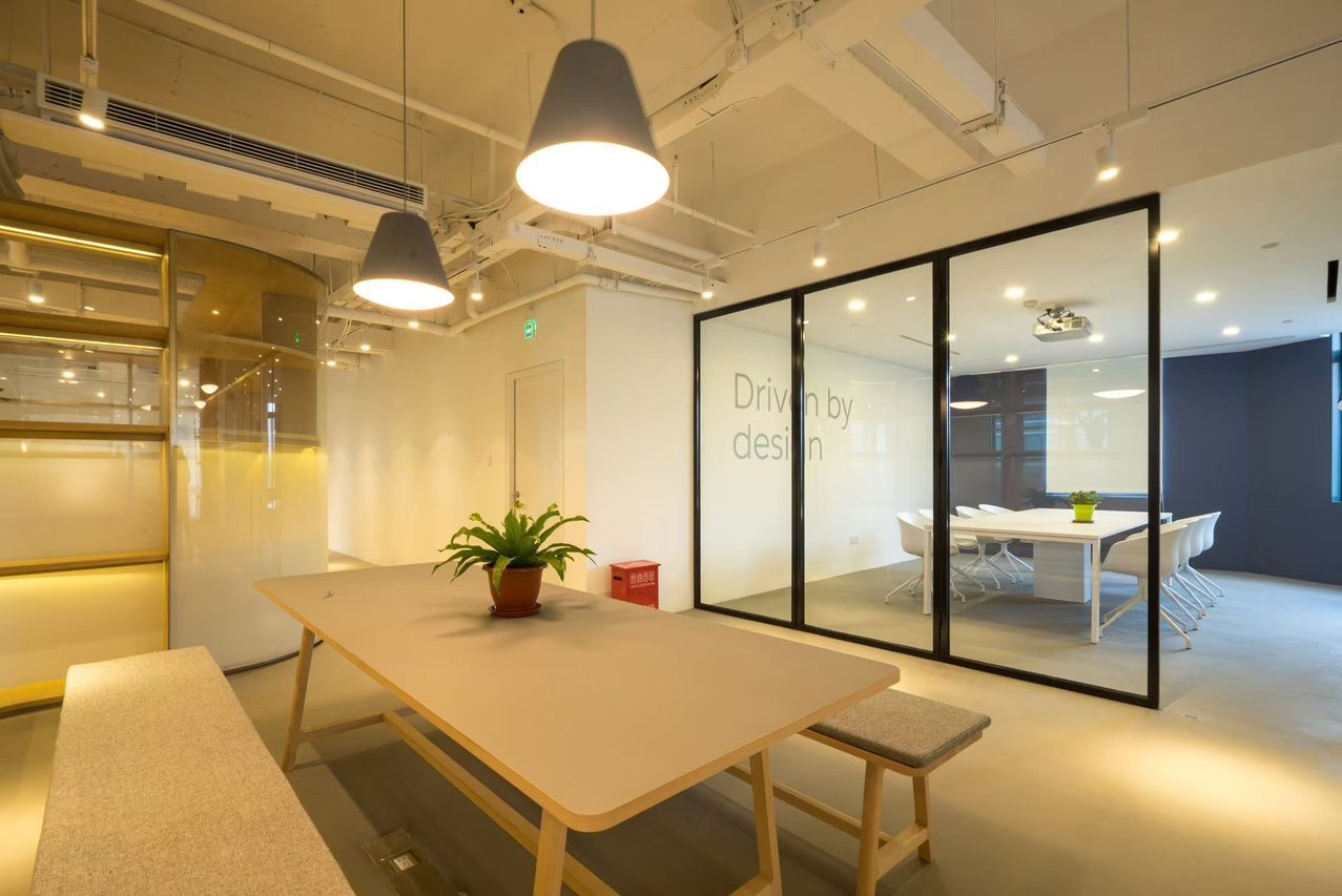 Nowoczesne biuro z przeszkloną ścianą działową i stołem konferencyjnym. Widoczny projektor na suficie i minimalistyczne oświetlenie.