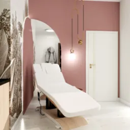 Nowoczesny gabinet kosmetyczny z białym fotelem zabiegowym na tle ściany w odcieniach różu i widokiem na miasto przez duże okno. Elementy dekoracyjne w kolorze złota.