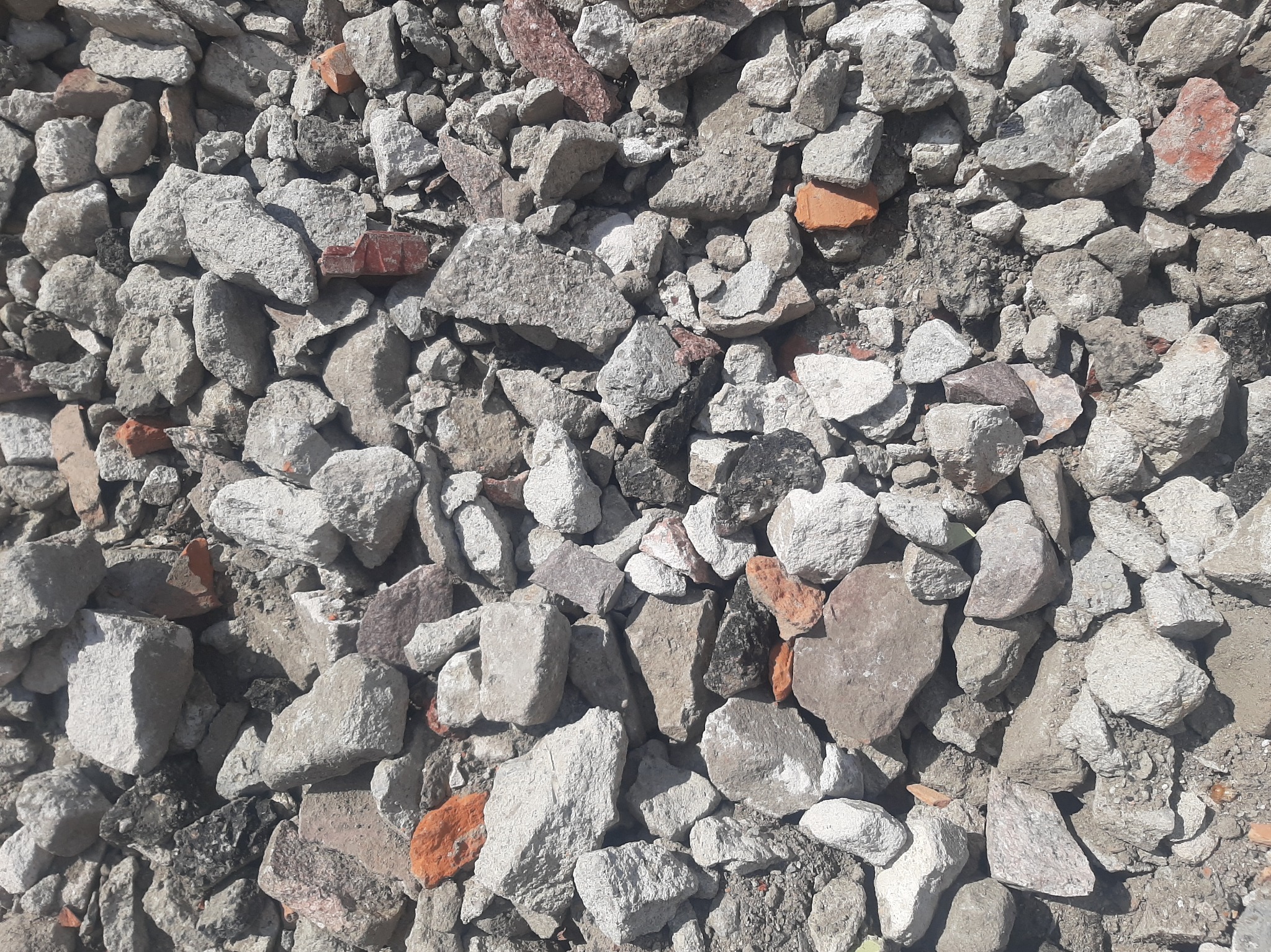 Gruz budowlany z fragmentami cegieł w zbliżeniu. Szare kamienie i czerwone cegły tworzą mieszankę. Widoczne ślady ziemi. Drobny materiał po rozbiórce.