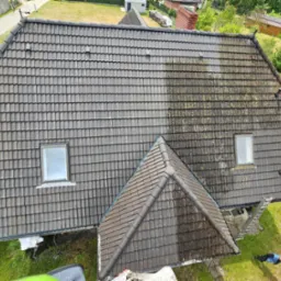 Czyszczenie dachu z dach&oacute;wki: połowa dachu umyta, druga pokryta mchem i zabrudzeniami. Widoczna drabina i myjka ciśnieniowa na trawie.