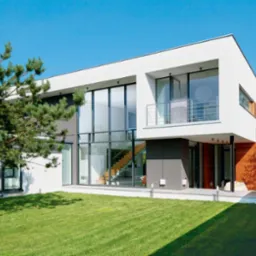 Nowoczesny dom z dużymi przeszkleniami i drewnianymi elementami elewacji, jasne tło nieba, widok z zewnątrz na schody wewnątrz.