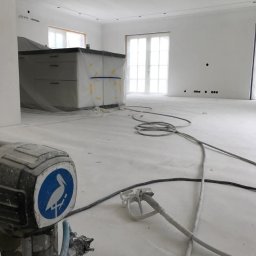 Malta - Wnętrze po malowaniu natryskowym: białe ściany, zakryta folią wyspa kuchenna, przewody i urządzenie do malowania na podłodze. Widoczne punkty świetlne w suficie.