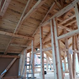 Malta - Wnętrze domu w trakcie budowy szkieletowej z widoczną drewnianą konstrukcją dachu, ścian i podłogi. Na podłodze stoi drabina, a w tle widać budynki.