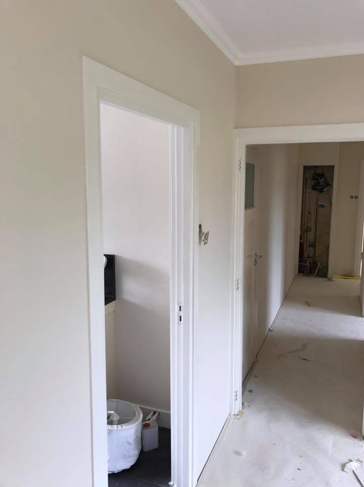 Korytarz po odświeżeniu: świeżo pomalowane ściany w beżowym odcieniu, białe futryny drzwiowe i listwy przypodłogowe. W tle widoczne dalsze pomieszczenia w trakcie prac.