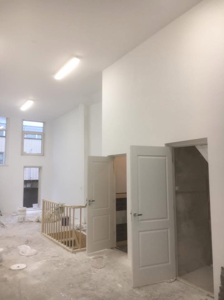 Wnętrze po remoncie: białe ściany, dwoje otwartych drzwi, drewniana balustrada schodów. Widoczne ślady po pracach wykończeniowych.