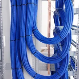 Równolegle ułożone, niebieskie przewody elektryczne spięte czarnymi opaskami w szafie sterowniczej z szyną uziemiającą. Estetyczny układ kabli.